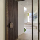 Large iron pivot door with vertical slats and a round handle, opening into a modern, light-filled entry with a sleek, minimalist design.