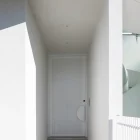 A minimalist white entry door with a circular cutout, framed by smooth white walls and a simple pathway, showcasing modern architectural design.
