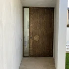 Bespoke iron pivot door with a textured surface and round handle, set against a white wall and leading to a landscaped outdoor area.