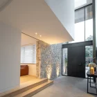 Modern entryway featuring a black iron hinge door, stone wall, wooden steps, and soft lighting, creating a warm, inviting atmosphere.