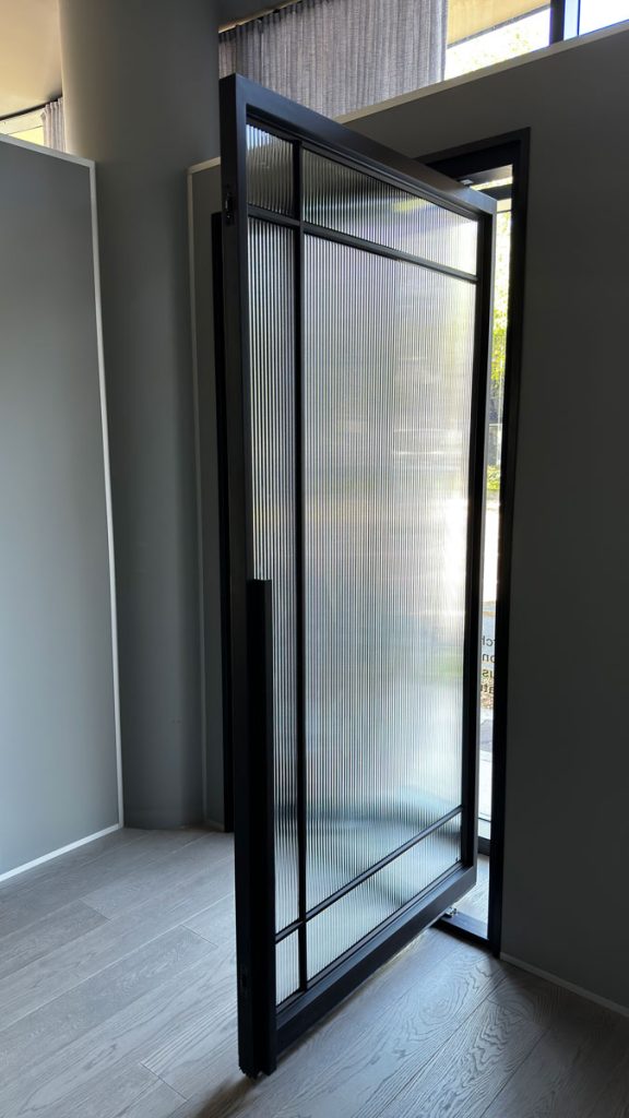 Bespoke Steel Door with Glass Panels in Modern Showroom Setting Bespoke steel door with a ribbed glass panel, slightly open, framed in sleek black, set within a modern showroom space.