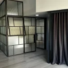 Steel-framed fixed windows with textured glass, arranged in an abstract pattern, set against a neutral wall and a dark curtain.