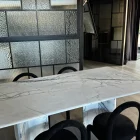 Marble dining table with curved black chairs against a backdrop of sleek steel-framed glass panels in a contemporary interior.