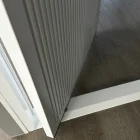 Close-up of a sleek, grey iron batten pivot door partially open, revealing a wooden floor and a modern glass panel in the background.