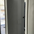 Grey iron pivot entry door with vertical ribbed design, set within a light-coloured frame, showcasing a modern interior space.