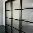 Black steel-framed sliding doors with textured glass panels, set against a neutral wall, featuring contemporary minimalist design elements.