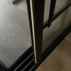 Black framed sliding door partially open, revealing textured glass and a sleek wooden floor. The design emphasizes modern aesthetics.