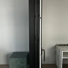 Steel frame sliding doors with a black finish, featuring a sleek handle, adjacent to a green marble pedestal and a white kitchen area.