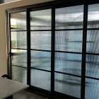 Black steel-framed sliding doors with textured glass, set against a light interior, showcasing a modern architectural design.
