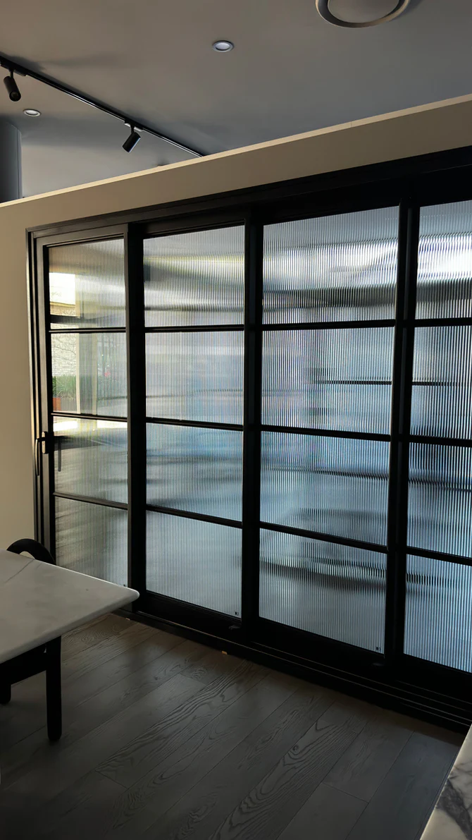 Black steel-framed sliding doors with textured glass, set against a light interior, showcasing a modern architectural design.