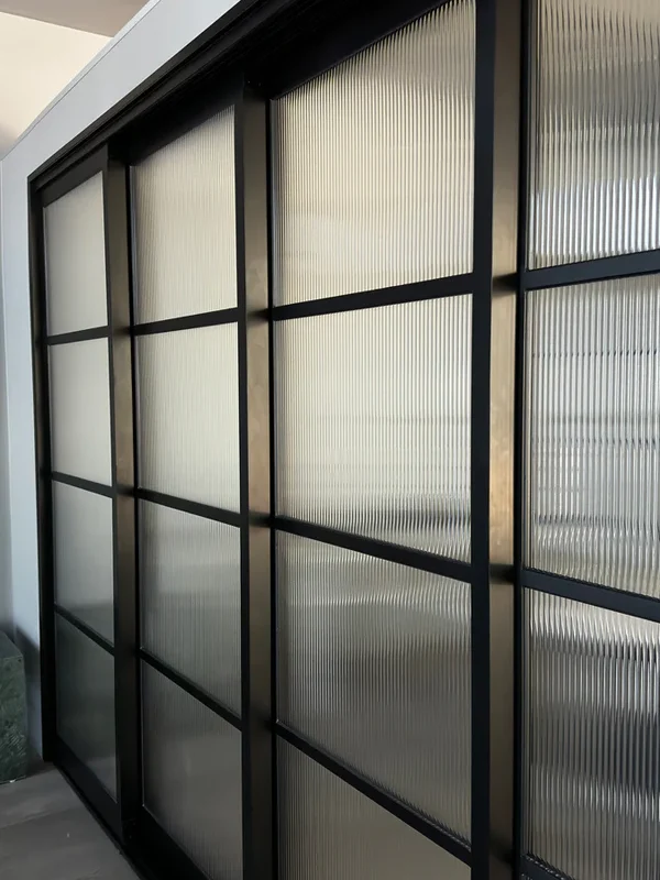 Steel-framed sliding doors with ribbed glass panels, featuring a sleek black finish, set within a modern interior space.