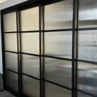 Black steel-framed sliding doors with textured glass panels, featuring a grid pattern, set against a modern interior backdrop.