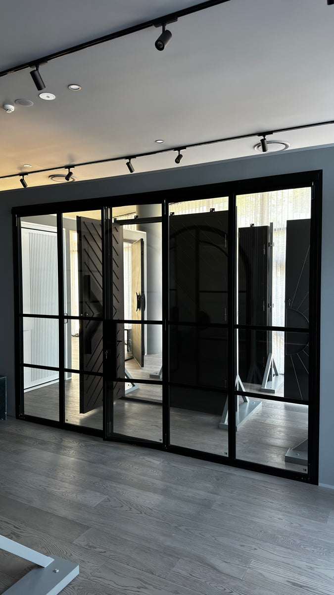 Elegant black steel bifold doors with large glass panels, set against a minimalist interior showcasing natural light and wooden flooring.