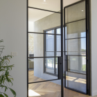 Black steel-framed glass doors open into a contemporary interior, showcasing a mix of natural light and sleek design elements.