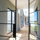 Steel-framed glass hinge doors open into a bright corridor with wooden flooring, showcasing natural light and modern architectural design.