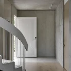 A contemporary hallway featuring a curved staircase, textured grey walls, and a white ribbed entry door with a circular handle.