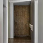 A sleek hallway featuring a textured iron batten entry door, accented by warm wooden flooring and minimalist light fixtures.