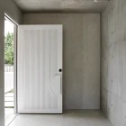 A modern entry door with a textured white surface is partially open, set against a minimalist concrete wall and light-toned flooring.