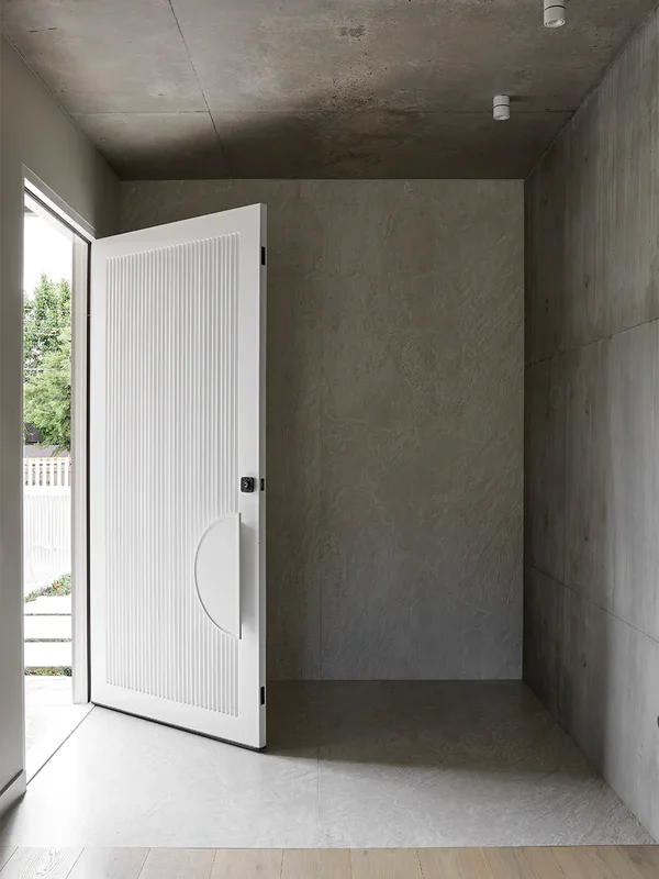 Bespoke white battened entry door partially open in a modern, minimalist space with concrete and wooden flooring.