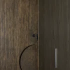Textured iron batten entry door with a circular handle, featuring a rich bronze colour, against a darker wooden backdrop.