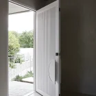 White iron batten door partially open, revealing a landscaped outdoor area through a modern entryway, with neutral-toned walls and floor.