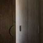 Sleek wooden doorway with vertical grooves, featuring a circular inset handle and adjacent smooth cabinetry, softly lit for emphasis.