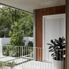 Bespoke iron entry door with vertical slats, framed by wooden accents and greenery, set against a modern concrete structure.