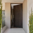 Stylish iron batten entry door with a textured dark finish, set in a modern entrance flanked by trimmed green plants and neutral walls.