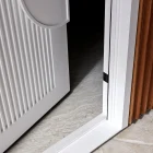 Close-up of a white entry door with vertical ridges, featuring a rounded handle, set against a textured stone floor and wooden frame.