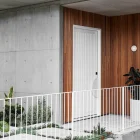 White iron batten hinge door set against textured wooden and concrete walls, with a planted garden and railing in the foreground.