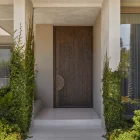 Bespoke iron entry door with textured finish, framed by lush greenery and minimalist steps, complementing a modern architectural design.