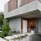 Contemporary building featuring a concrete exterior, wooden slats, a white door, and landscaped pathway with greenery.