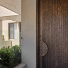 Bespoke galvanised iron batten hinge entry door with a textured bronze finish, set in a modern architectural space with greenery.