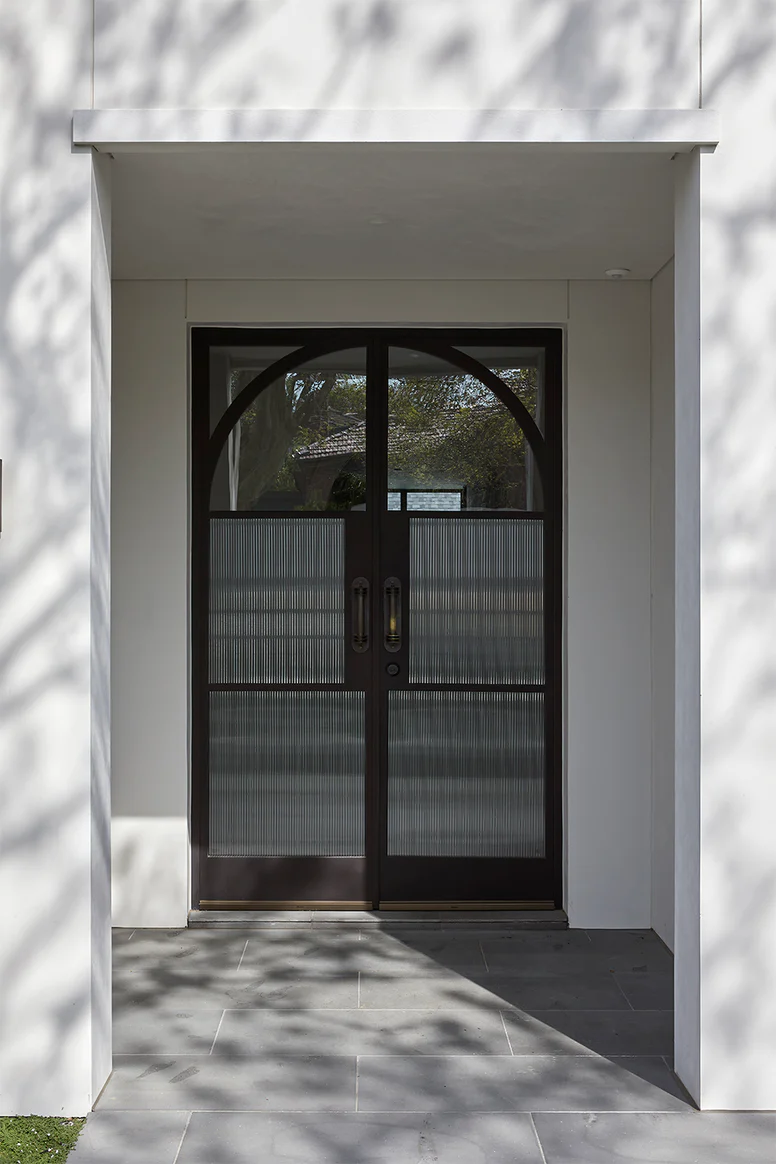 Stylish black steel-framed double doors with arched glass panels, set against a white wall and paved entranceway.