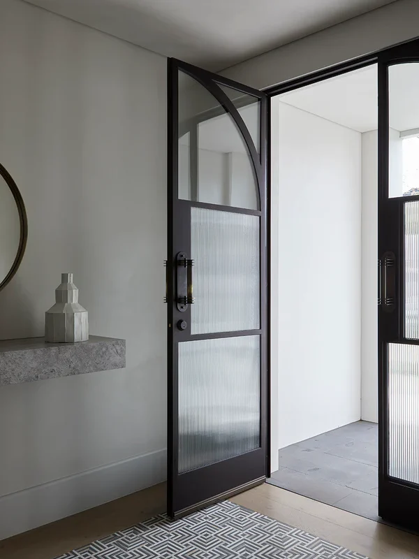 Bespoke arch steel door with glass panels, framed in black, set in a minimalist entryway with light walls and soft flooring.