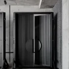 Bespoke iron batten entrance doors with a circular handle, set against a minimalistic concrete backdrop and textured grey drapery.