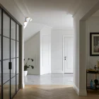 Modern hallway featuring a glass door with a black frame, herringbone wooden floor, and minimalist decor in neutral tones.