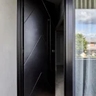Sleek black iron entry door with a geometric design, set within a contemporary frame, adjacent to glass panels and soft curtains.