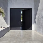 Elegant black iron batten hinge entry doors open to a stylish concrete entryway, framed by modern grey walls and a sculptural tree.