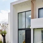 Modern architectural entry featuring a black iron hinge door, large windows, wooden accents, and a landscaped garden.