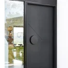 Sleek black iron entry door with a circular handle and diamond-shaped design, set against a glass panel and modern interior.