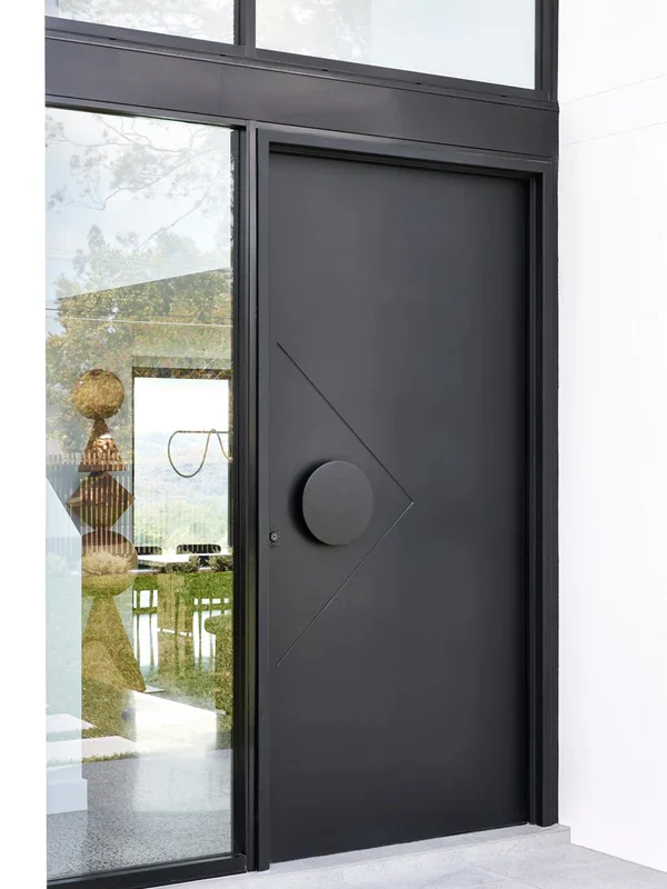 Sleek black iron entry door with a circular handle and diamond-shaped design, set against a glass panel and modern interior.