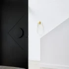 Sleek black iron entry door with a circular handle, opening to a bright interior featuring white walls and modern decor.
