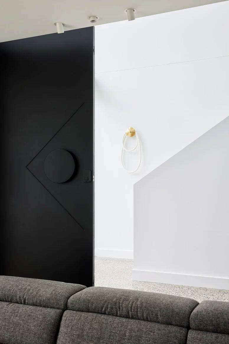 Sleek black iron entry door with a circular handle, opening to a bright interior featuring white walls and modern decor.