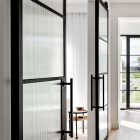 Internal view of sleek galvanised steel frame glass barn sliding doors, featuring textured glass panels and modern black handles, framed by light wood flooring.