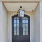 Elegant double-entry door with black wrought iron hinges and glass panels, flanked by a stylish lantern, set against a creamy stone façade.