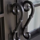 Black wrought iron hinges with elegant curled designs, affixed to a sleek, contemporary entry door with glass panels.