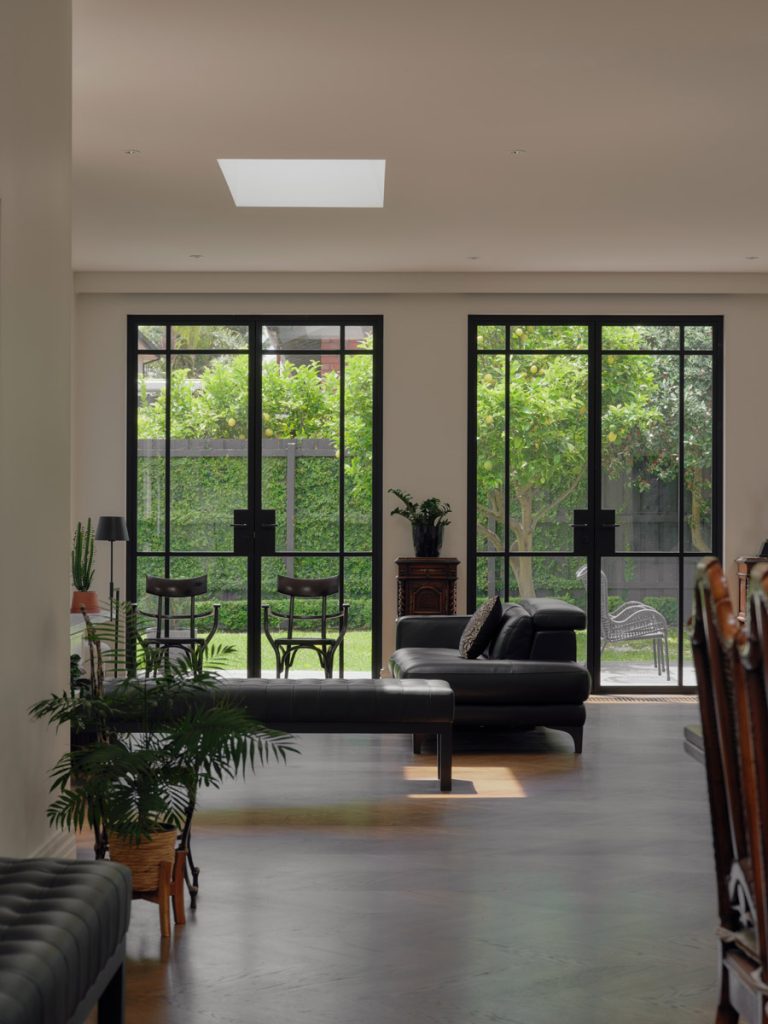 Bright living space featuring black steel-framed doors opening to a lush garden, with modern furniture and green indoor plants.