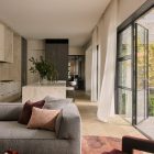 Elegant living space featuring a grey sofa with burgundy cushions, light curtains, and large glass doors opening to a garden.