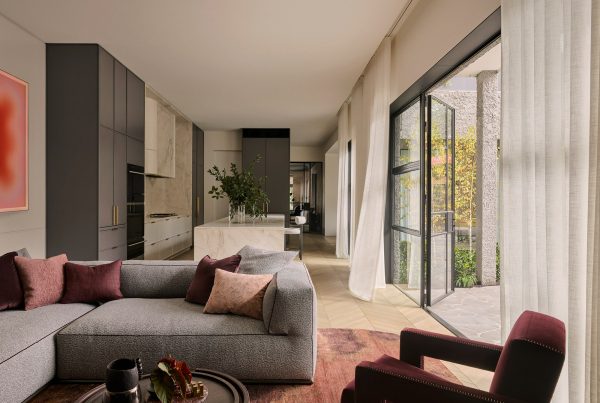 Modern lounge featuring a grey modular sofa, burgundy accents, and large glass doors opening to a landscaped outdoor area.